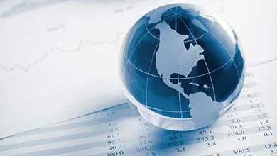 A blue glass globe, depicting the Americas, sits atop a financial document filled with columns of numbers and a subtle line graph.