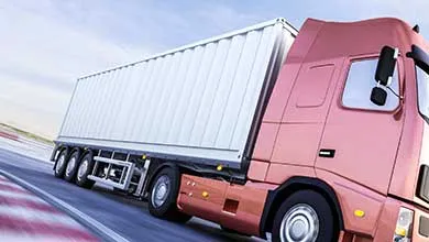Low-angle, close-up of a moving reddish-pink semi-truck with a white trailer on a road.