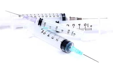 Three clear medical syringes with needles and black scale markings on a white surface.