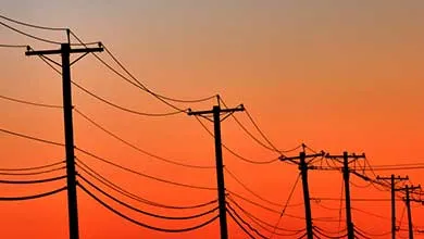 Silhouetted utility poles and power lines against an orange sunset.