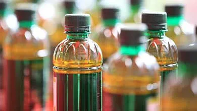Close-up of plastic bottles filled with golden-yellow liquid, each with a black cap and green ring. One bottle is sharply focused in the foreground; the others are blurred in the background.