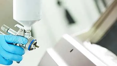 Technician operating a spray application system with connected hose and material cup in an industrial environment.