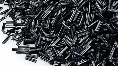 Close-up of black chopped long fiber thermoplastic pellets scattered on a white surface.