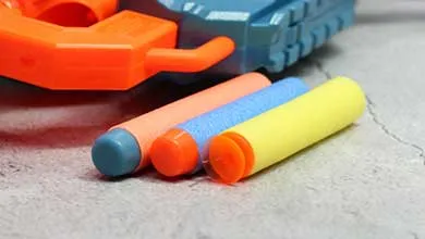 Close-up of a blue and orange toy gun with several colorful foam darts lying in front on a gray surface.