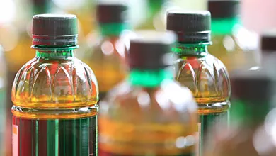 Close-up of small plastic bottles with green textured necks, black caps, and filled with golden-yellow liquid.