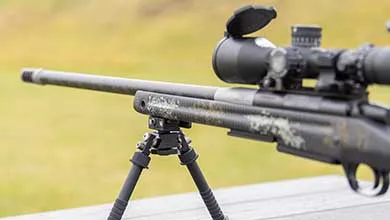 Close-up of a camouflage-patterned rifle on a bipod with a large scope attached.
