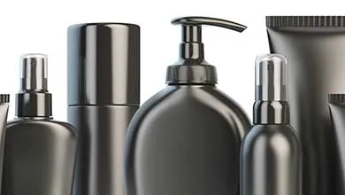 Assortment of matte black cosmetic packaging containers, including bottles, pumps, and tubes, arranged on a white background.