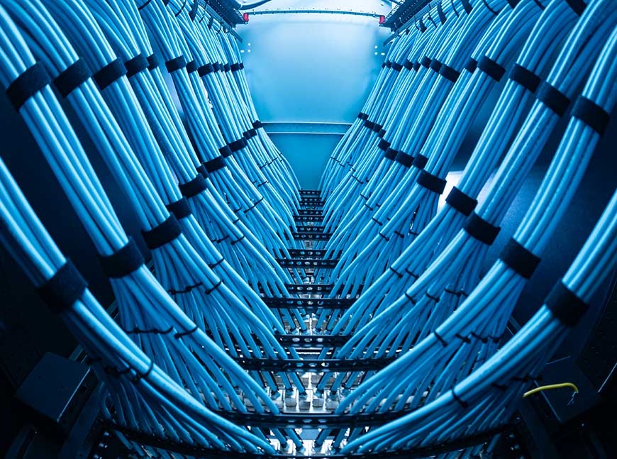 Low-angle view of two symmetrical rows of bright blue network cables, neatly bundled with black straps inside a server rack.